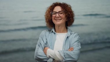 Orta yaşlı, esmer, kıvırcık saçlı ve gözlüklü İspanyol kadın kollarını çapraz bir zemine dayamış gülümsüyor, kendine güveni ve sıcaklığıyla..