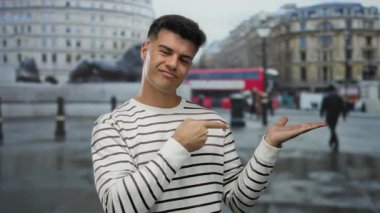 Şehir arka planında bulanık şehir arkaplanını gösteren, çizgili gömlek giyen, açık havada kendine güveni ve çekiciliği olan genç bir adam..