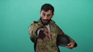 Sakallı İspanyol üniformalı adam yeşil arka planda ileriye bakan miğfer tutuyor..