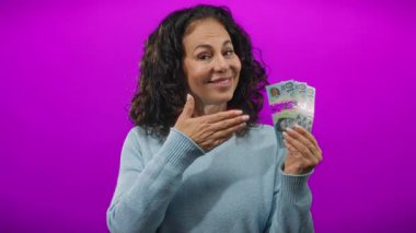 Avustralya banknotları tutan ve mutlu bir gülümseme ve günlük kıyafetle mor bir arka plana baş parmak işareti yapan kadın, mali açıdan memnuniyet ve pozitiflik gösteriyor..