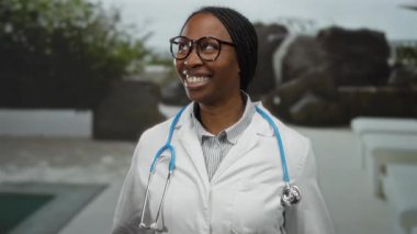 Açık havuz başında steteskopla gülümseyen bir kadın açık havuz başında yeşil zeminli bir hastane ortamında rahat bir sağlık ortamı öneriyor..