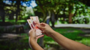 Bir açık hava parkında Norveçli Krone banknotları tutan bir adam, para işleme vurgulayan bir şehir ortamında finans ve yatırım odaklı.