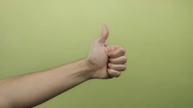 Beyaz adam sarı bir duvara başparmak gösteriyor, izole ve canlandırıcı, pozitifliği ve onayı minimalist bir arka planda yakalıyor ve el hareketlerine odaklanıyor..