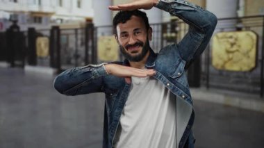 Sakallı İspanyol bir adam, güneşli bir günde neşe ve coşku ifade eden, arka planı bulanık kot ceketli, şehir sokaklarında heyecanlı bir şekilde el kol hareketi yapıyor..