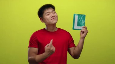 Kırmızı tişörtlü genç adam parlak sarı bir arka plana karşı öğrenci tabelasını işaret ediyor, motivasyon ve coşku hissi uyandırıyor..