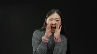 Siyah arka planda sıcak süveter giyen, uzun saçlı, neşeli yüzlü, neşeli bir kadın tezahürat ve coşkuyla bağırıyor..