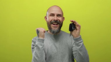 Başarıyı kutlayan adam, sarı arka planda izole edilmiş araba anahtarlarıyla mutluluk ve başarı sergiliyor..