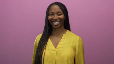 Sarı gömlekli, uzun örgülü, pembe bir duvara gülümseyen bir kadın canlı, izole bir arka planda mutluluk ve tarz sergiliyor..