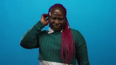 Mavi arka planda yeşil süveter giyen pembe örgülü kadın izole edilmiş portre ortamında düşünceli ve düşünceli görünüyor..