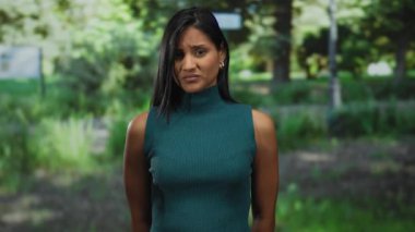 Parktaki genç bir kadın, güneş ışığı ağaçların arasından süzülüp doğal bir huzur ortamı yaratırken,... dışa vurumu onaylamayarak el kol hareketi yapıyor..