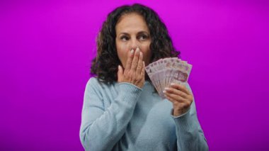 Mor arka planda Meksika pezosu tutan orta yaşlı bir kadın elinde banknotlarla şaşırmış görünüyor, izole bir ortamda zenginlik ve duyguyu ön plana çıkarıyor..
