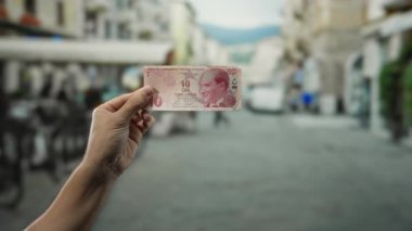 Açık şehir sokak ortamında Türk lirası banknotunu tutan adamın eli, canlı bir günde kentsel yaşam ve para kullanımını yakalıyor.