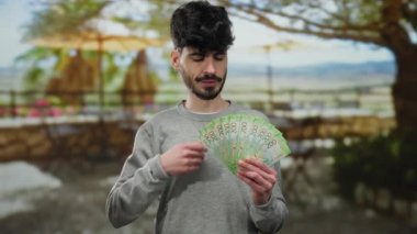 Parkta elinde Rus rublesi banknotlar tutan bir adam. Ağaçları ve arka planı bulanık. Açık havada mutluluk ve kendine güveni ifade ediyor..