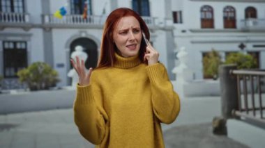 Binanın dışında telefonla konuşan, sarı kazak giyen, şehirde duygularını ifade eden, iletişim yaşam tarzını ve şehir deneyimini sembolize eden bir kadın.