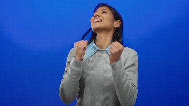 Neşeli mavi arka planda kutlama yapan bir kadın, neşeli bir ifadeyle mutluluk ve başarıyı ifade ediyor..