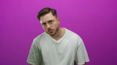 İzole edilmiş, pembe arka planı olan sakallı genç bir adam beyaz tişört giyiyor.