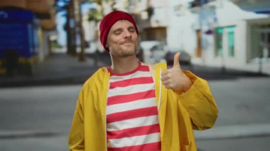 Sarı ceketli genç adam, şehir arka planına karşı olumlu bir tutum ve neşeli bir tavır sergiliyor..