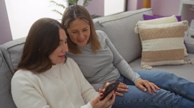 Anne ve kız kanepede bir tabletle vakit geçiriyorlar. Evdeki aile sevgisini ve bağlantısını temsil eden samimi bir iç mekan ile çevrili..