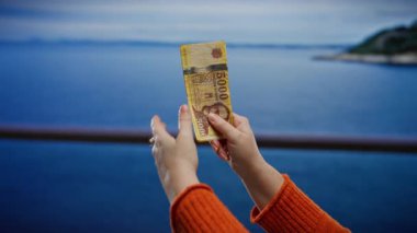 Bir kumsalda elinde Macar banknotları tutan bir kadın mavi gökyüzünün altında para sergiliyor..