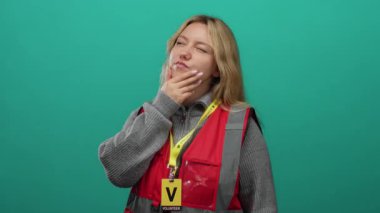 Yeşil arka planda gönüllü olan kırmızı yelekli bir kadın.