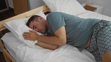 Yatak odasında uyuyan bir adam pijamalı bir kadın gibi onu battaniyeyle örterek ev içi huzuru yansıtıyor..