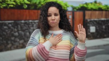 Genç İspanyol kadın, güneşli bir sokakta renkli bir kazak giyerek yemin ediyor.