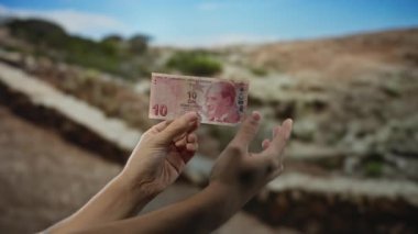 Mavi gökyüzünün altındaki bulanık açık hava parkına karşı elinde 10 lira banknot tutan adam..