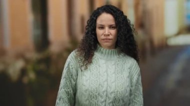 Sakin bir sokakta rahat bir kazak giyen kadın, sakin bir ifadeyle ve açık havada yumuşak, kıvırcık saçlarıyla durgun bir hava yayıyor..