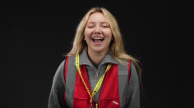 Siyah arka planda kırmızı yelekli, beyaz tenli, genç ve enerjik sarışın bir kadın, yardımsever bir ortamda gençlik ve enerji taşıyor..
