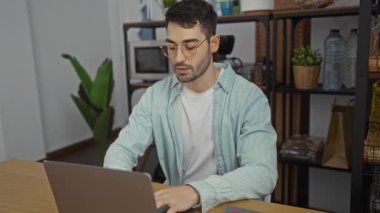 Modern ofiste dizüstü bilgisayarda çalışan genç bir adam. Fabrikaları ve rafları var. Çalışma alanlarını ve profesyonel ortamları gösteriyor.