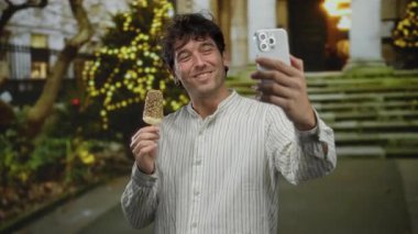 Dondurma yerken gülümseyen ve şenlikli ışıklarla çevrili sokakta selfie çeken İspanyol bir adam..