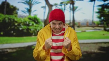 Sarı ceketli ve kırmızı bereli genç adam gün boyunca açık hava parkında mutluluğunu ifade ediyor..