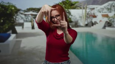 Oteldeki havuzun yanında gülümseyen bir kadın elleriyle yüzünü çerçeveliyor ve rahat bir atmosfer yaratıyor..