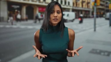 İnsanlar ve araçlar arka planda hareket ederken İspanyol genç kadın kentin işlek caddesinde güvenli bir şekilde dikiliyor ve canlı şehir atmosferini yakalıyor..