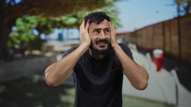 Sakallı İspanyol bir adam, güneşli bir çevrede sokakta hayal kırıklığına uğramış görünüyor..