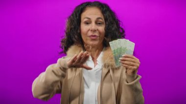 Romen banknotlarını elinde tutan orta yaşlı bir kadın canlı bir mor arka plana karşı, neşeli bir ifadeyle para sergiliyor..