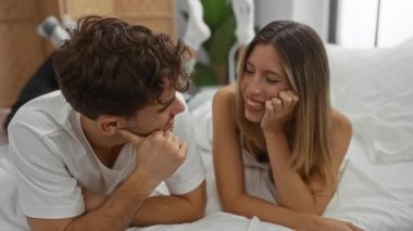 Yatak odasında uzanan çift mahrem bir anı paylaşıyor, kadın ve erkek kapalı alanda gülümsüyor, aşkı, ilişkiyi, ev ortamını ve bağlantıyı tasvir ediyor..