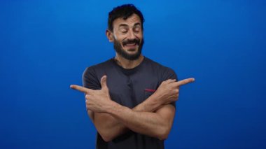 Günlük gömlekli İspanyol bir adam gülümsüyor ve parlak mavi bir arkaplanı işaret ediyor. Olumlu duygular ve gelişigüzel davranışlar sergiliyor..
