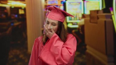 Pembe mezuniyet elbisesi giymiş genç bir kadın kumarhane makinesinin arka planına şaşırdı. Beklenmedik bir kutlama ya da servet öneriyor..