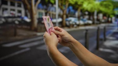 Bir şehir caddesinde Meksika pesosu tutan adam, şehir dışı ticaret havası sergiliyor..