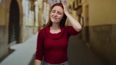 Şehir caddesinde dikilen kızıl saçlı kadın, günlük giysiler giyiyor, tarihi mimarinin tanımladığı şehir ortamında duygularını ve düşünceli bir şekilde ifade ediyor..