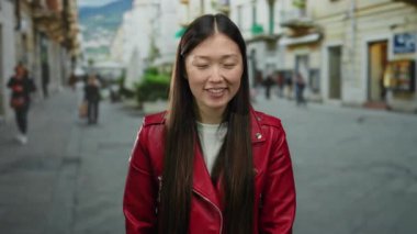 Kırmızı ceketli bir kadın arka planı bulanık, şehir yaşamını ve enerjik enerjisini gösteren hareketli bir caddede gülümsüyor..