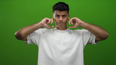 Yüzünde yeşil arka planda kulakları kapatan beyaz tişörtlü genç adam izole edilmiş.