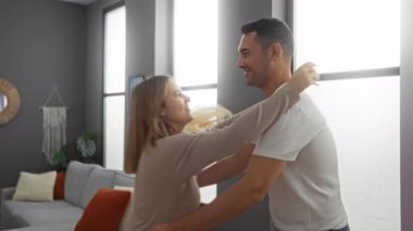 Sıcak oturma odasında kucaklaşan çift modern iç tasarım ve geniş pencerelerden gelen yumuşak doğal ışık ile çevrili sıcak bir romantik an yaratıyor.