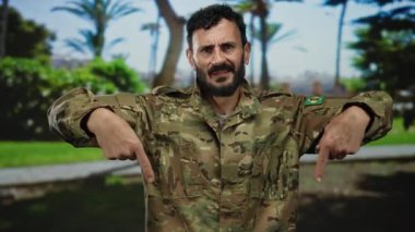 Sakallı, askeri üniformalı İspanyol bir adam arka planda ağaçlarla güneşli yeşil bir parkın aşağısına işaret ediyor..