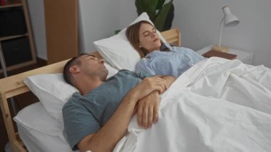 Yatak odasında uyanan çift, yatakta yatan kadın ve erkek, evin içinde sıcak bir sabah, beyaz çarşaflar ve yumuşak ışıklandırmayla huzurlu ve samimi bir ortam..