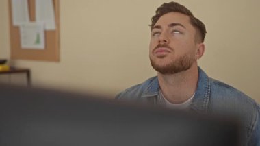 Ofiste sakallı genç bir adam içeride otururken düşünceli görünüyor, iş yerinde bir anlık tefekkür sergiliyor..