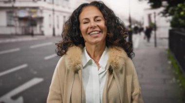 Şehir sokaklarında gülümseyen ve parmakla işaret eden kadın, kışın giydiği kıyafetle mutluluk ve kendine güveni somutlaştırıyor..
