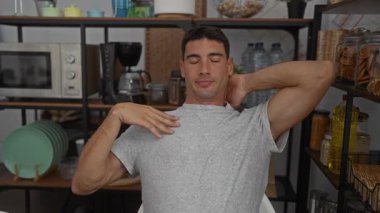 Adam rahat bir ofis mutfağında, kolları başının arkasında, raflar, bulaşıklar ve mikrodalga fırınla çevrili, sakin ve rahat bir atmosfer yaratıyor..