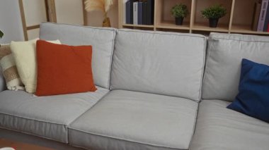 Genç adam modern oturma odasındaki kanepede rahat bir ev ortamı öneren şık dekorasyon bitkileri ve minderlerle dinleniyor..